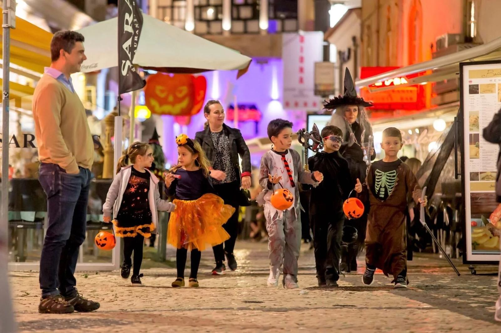 Children in Halloween costumes with pumpkin buckets on a street in Albufeira old town at night