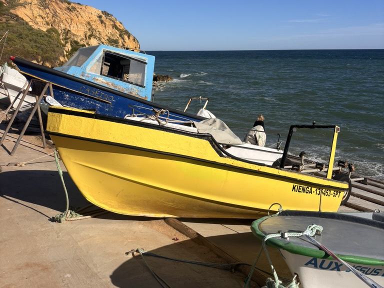 Yellow and blue fishing boat pulled up on the sand below the cliffs at Olhos de Água, Albufeira