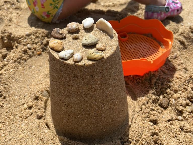 Child building a sandcastle decorated with pebbles on Santa Eulália Beach in Albufeira